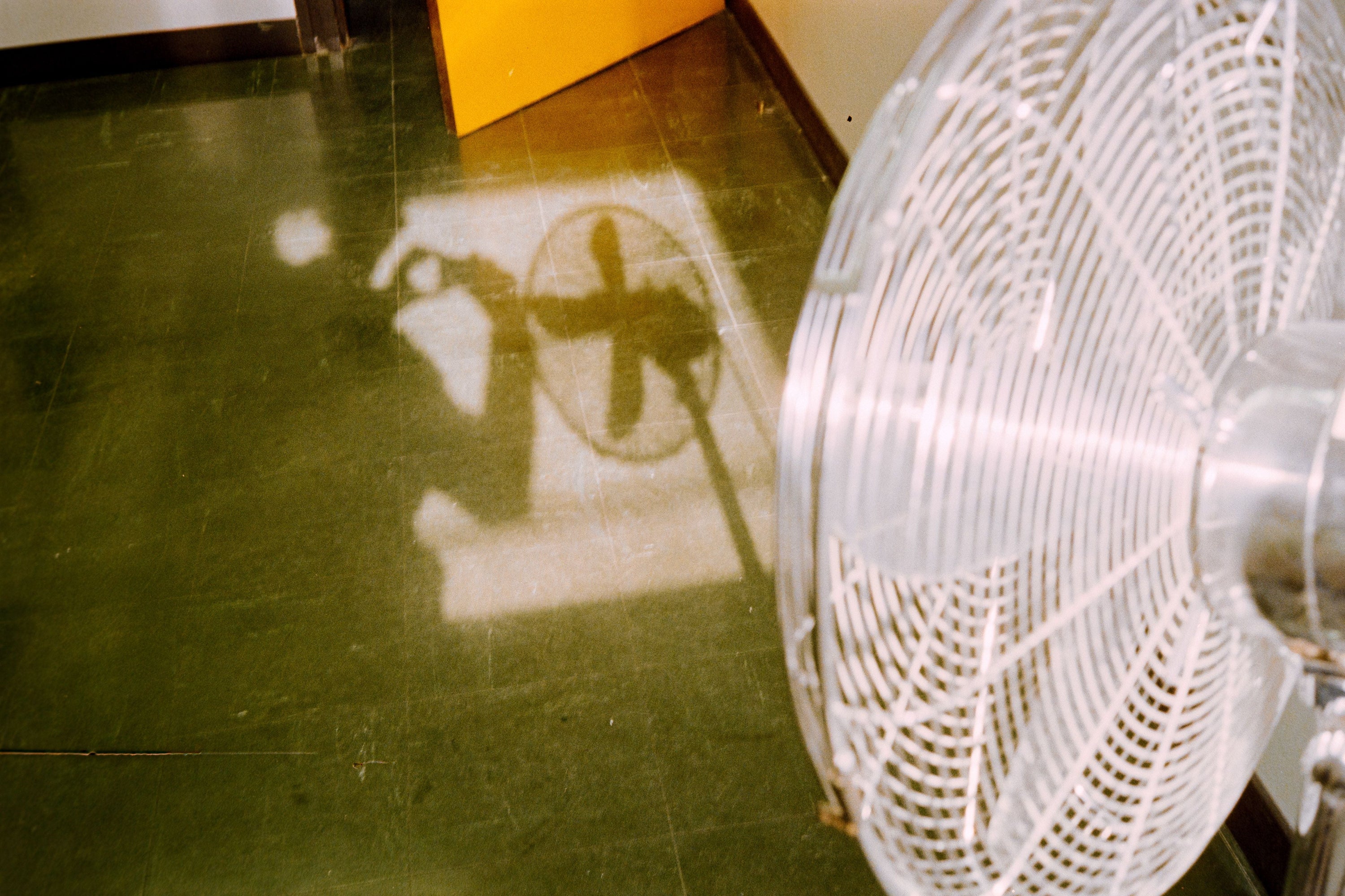 Interesting shadow of a fan casting on a green floor with an open door.